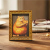 A framed painting of an orange cat eating pizza, displayed on a wooden surface.