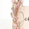 A pink buttercream cake decorated with delicate, gold-edged butterfly toppers and pearl accents.