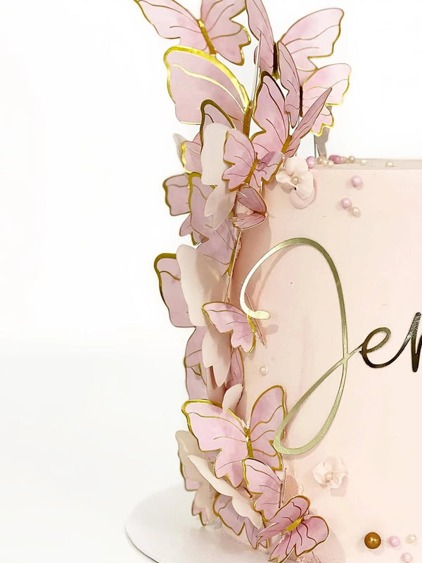 A pink buttercream cake decorated with delicate, gold-edged butterfly toppers and pearl accents.
