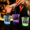 A hand pours a liquid into a glass of LED light-up shot glasses for parties.