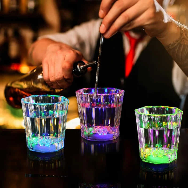 A hand pours a liquid into a glass of LED light-up shot glasses for parties.