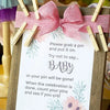 A wooden sign with a pink ribbon and text instructing guests to grab a pin for a celebration.
