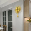 A round gold wall clock with Arabic numerals hangs on a white wall above a glass-paned door.