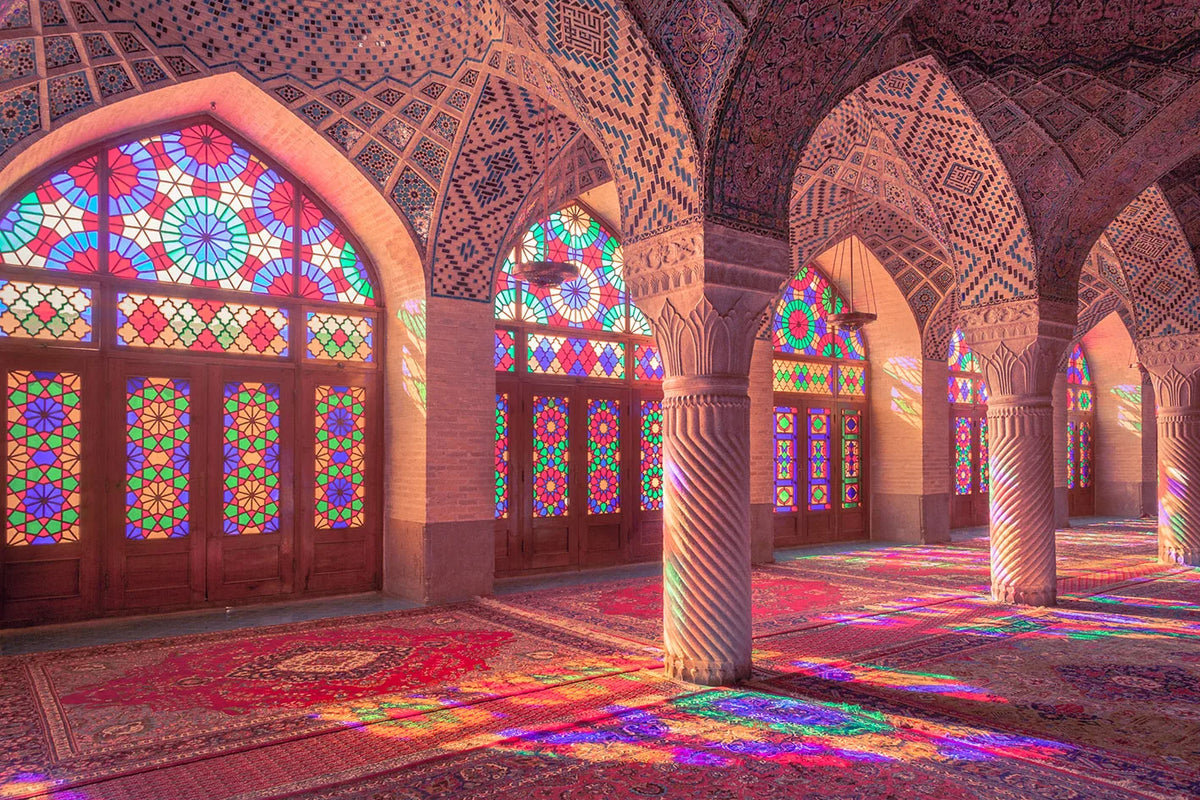 Interior view of an Islamic mosque with arched windows and colorful geometric patterns on the floor.