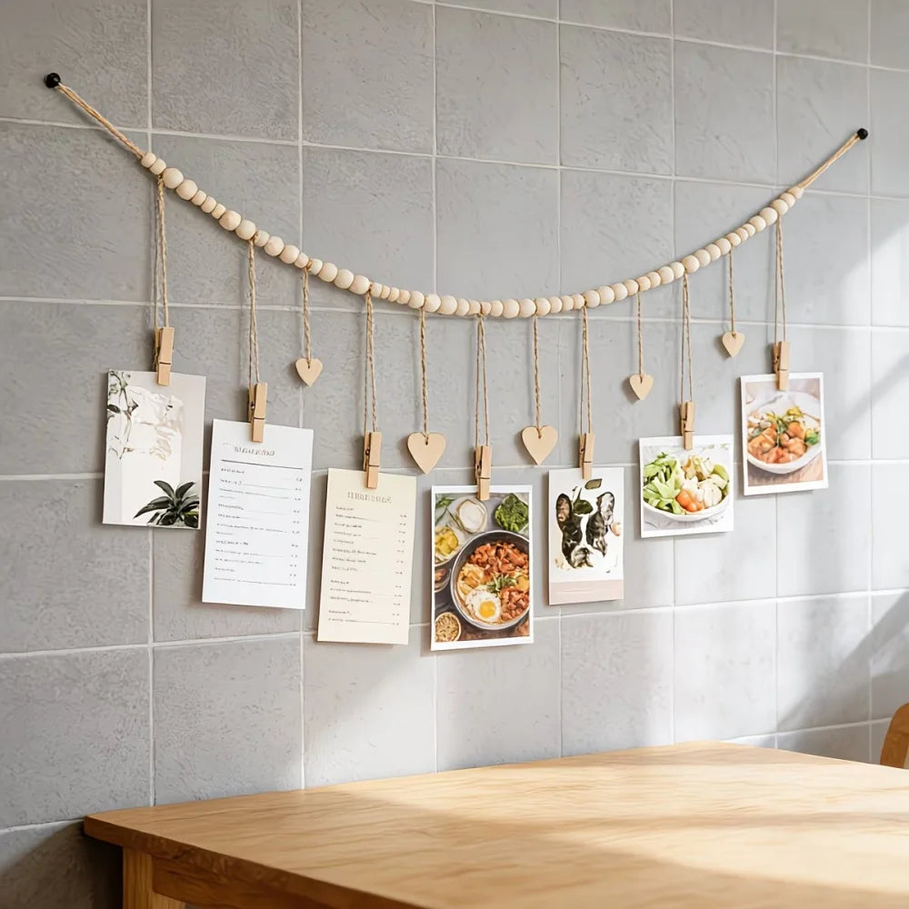 A beige beaded garland with wooden clips displays several framed photos and cards on a gray tiled wall.