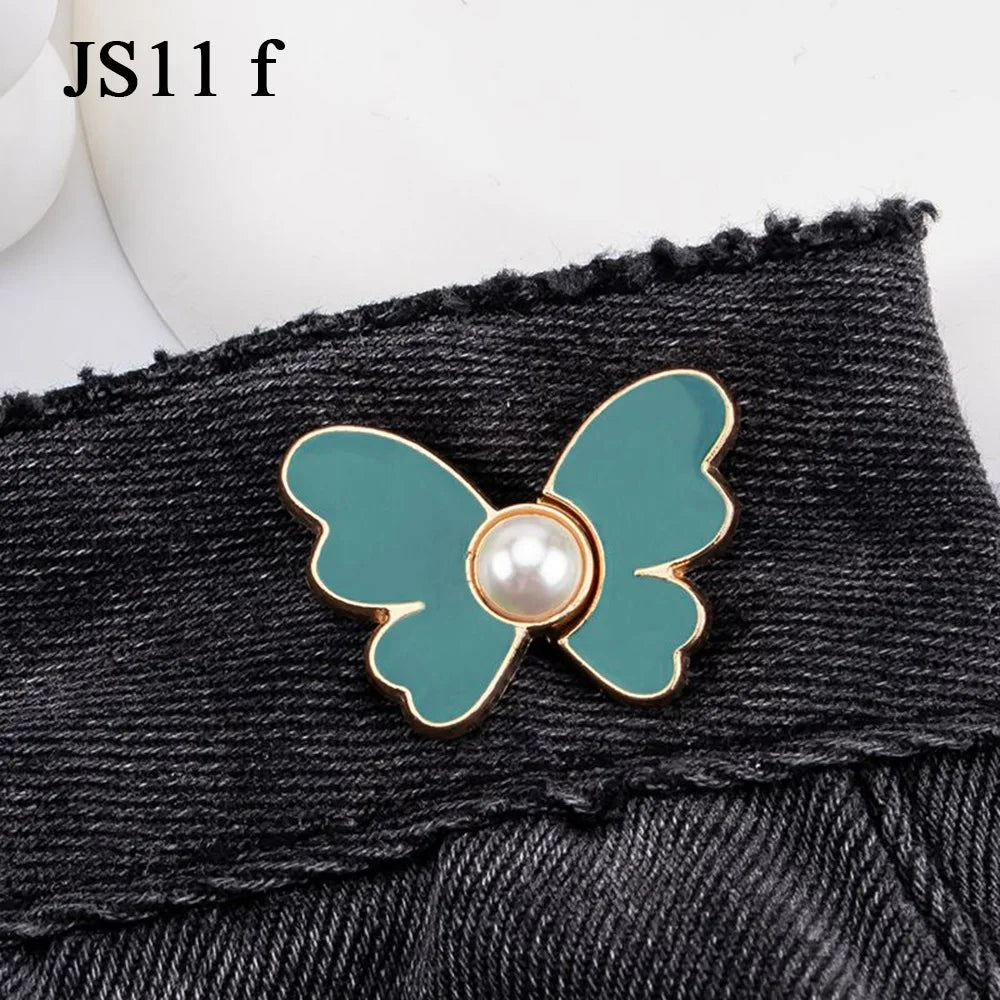 A teal butterfly button with a pearl center is attached to a black denim garment.