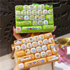 A hand holds a green cartoon animal keyboard keycap keychain with various colorful keycaps.