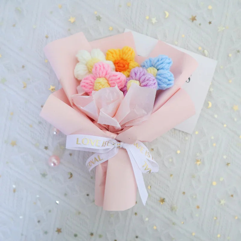 A handmade crochet sunflower mini bouquet featuring pink and yellow flowers tied with a white ribbon.