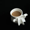 A white ceramic vase shaped like a vertebra holding a brown liquid.