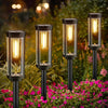 A row of black retro solar pathway lights illuminates a garden bed with pink flowers at night.