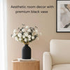 Aesthetic room decor featuring a large matte black vase filled with white flowers on a wooden table.