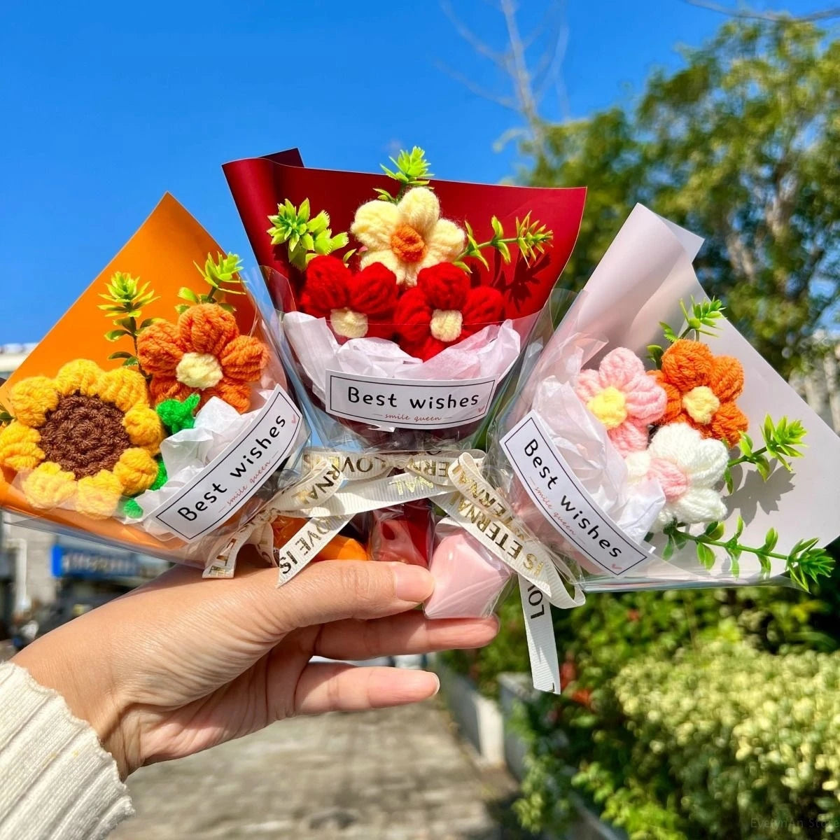 A hand holds a bouquet of handmade crochet flowers in various colored paper bouquets.
