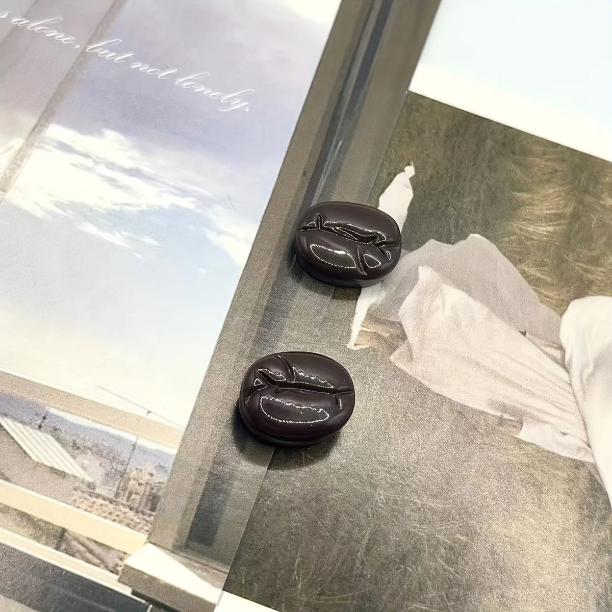 Un ensemble de deux aimants en forme de grains de café marron foncé, présentés sur une surface de verre.