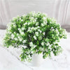 A bouquet of green artificial fern and leaf sprigs with white flowers displayed on a white marble surface.