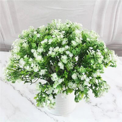 A bouquet of green artificial fern and leaf sprigs with white flowers displayed on a white marble surface.