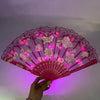 A pink LED dancing hand fan with floral patterns is held against a purple background.