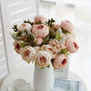 A bouquet of pink and peach peony artificial flowers with green foliage in a white vase.