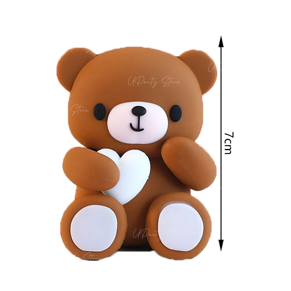 A cute brown teddy bear shaped cake topper with white accents and pink ball decorations.