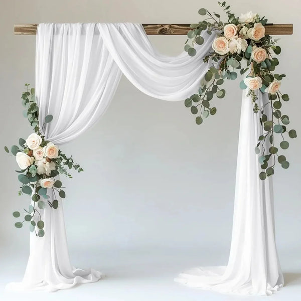 White sheer tulle draping fabric used to create a wedding arch backdrop with floral greenery