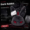 A dark gray rabbit plush toy with red eyes and a white bandage design, shown against a black background.