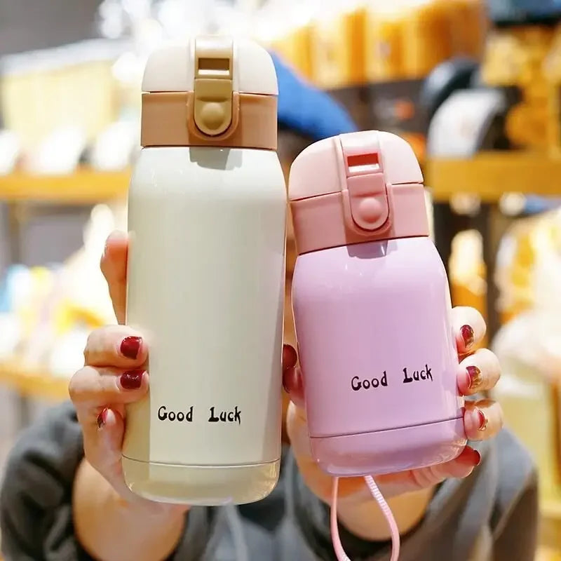 A hand holds a pink vacuum insulated coffee mug with Good Luck text on it.
