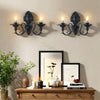 Vintage black wall pendant candle holders mounted above a wooden dresser with framed art.