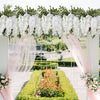 A white floral archway decorated with artificial wisteria vines and silk bloom forks in a garden setting.