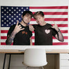 A man in a black shirt poses next to an American flag tapestry on a wall.