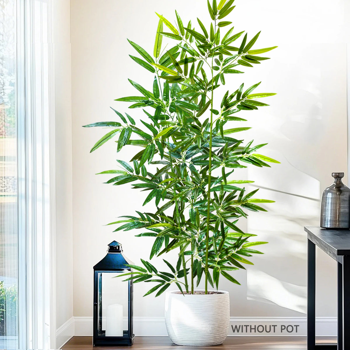 Artificial bamboo branch with green leaves displayed in a white pot next to a window.
