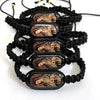 A black braided bracelet featuring multiple oval wooden charms depicting the Virgin Mary.