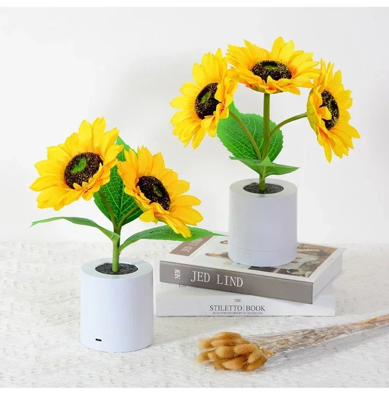 A bright yellow sunflower plant in a white pot with a black center, displayed on a white surface.