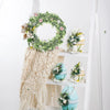 Étagère en bois blanc décorée d'une couronne d'eucalyptus vert et d'objets décoratifs blancs et bleus.