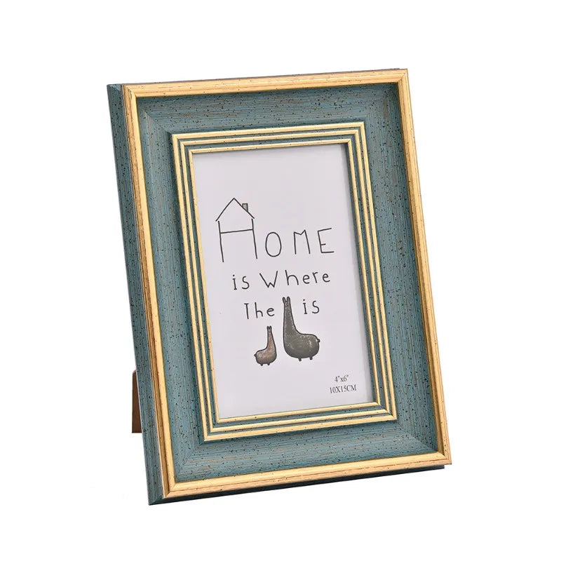 A rectangular wooden photo frame with a distressed teal border displaying the text Home is Where The Is and two small wooden 