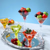 A collection of colorful fruit garnishes in clear plastic martini glasses displayed on a silver tray.