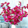 Leuchtend magentafarbene künstliche Bougainvillea-Blüten in einem weißen Topf vor blauem Hintergrund.