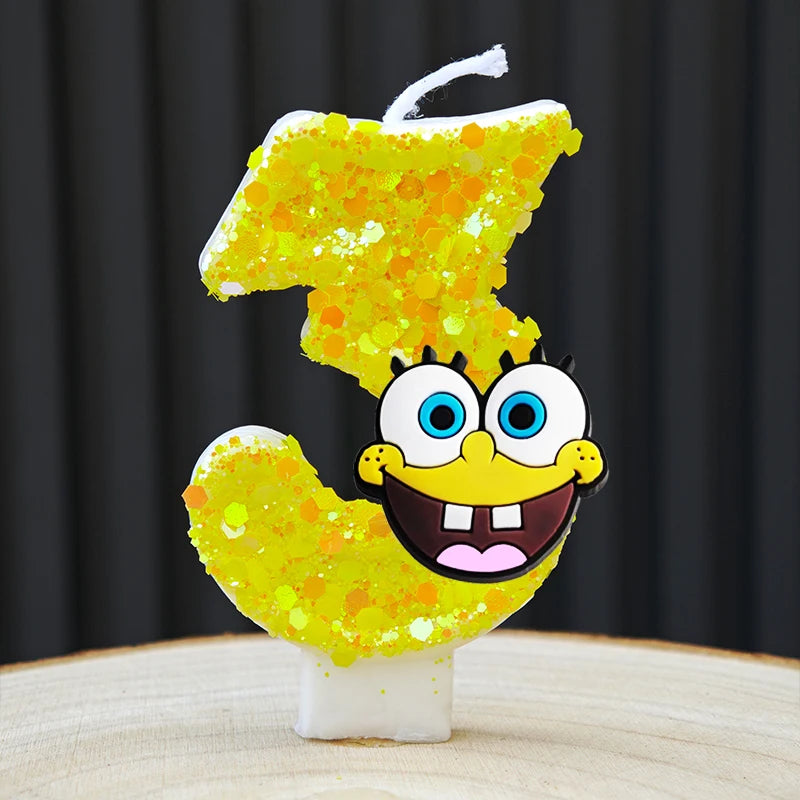A yellow sponge cake candle shaped like the number 3, decorated with yellow glitter and a face.