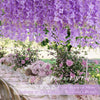 Purple artificial wisteria flower garland hanging outdoors in a garden setting.