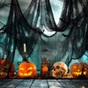 A spooky Halloween display featuring carved pumpkins, a skull, and dark gauze fabric against a blue sky background.