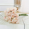 A bouquet of pale pink silk peonies with green stems displayed on a white surface.
