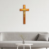 A wooden crucifix with a gold Jesus figure mounted on a light gray wall above a sofa.
