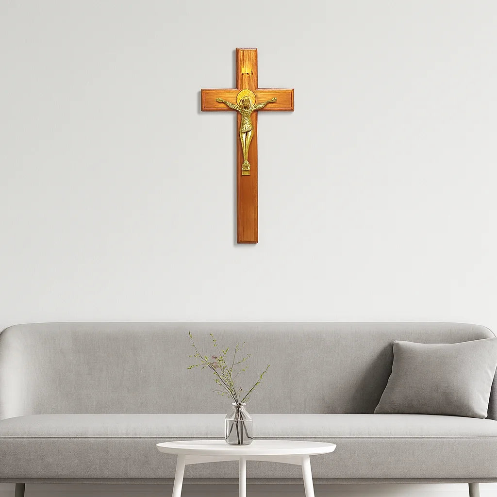 A wooden crucifix with a gold Jesus figure mounted on a light gray wall above a sofa.