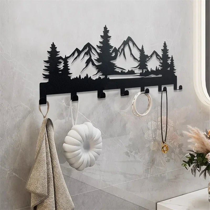 Black metal mountain forest silhouette key holder with hooks mounted on a white wall.