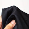 A hand is holding a black face mask surprise party prop made of mesh fabric.