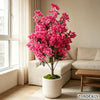 Leuchtend pinker künstlicher Bougainvillea-Baum in weißem Topf, drinnen neben Fenster und Sofa.