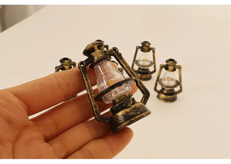 A hand holds a vintage ceramic miniature lantern with a glass bulb and brass fittings for dollhouse décor.