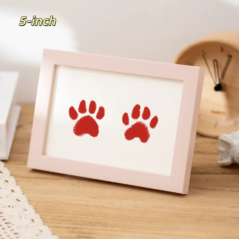 A pink 5-inch photo frame displaying two red paw prints on a wooden surface.