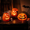 An orange glowing jack-o'-lantern decoration with a triple-layer design sits on a dark wooden surface next to skulls and spid