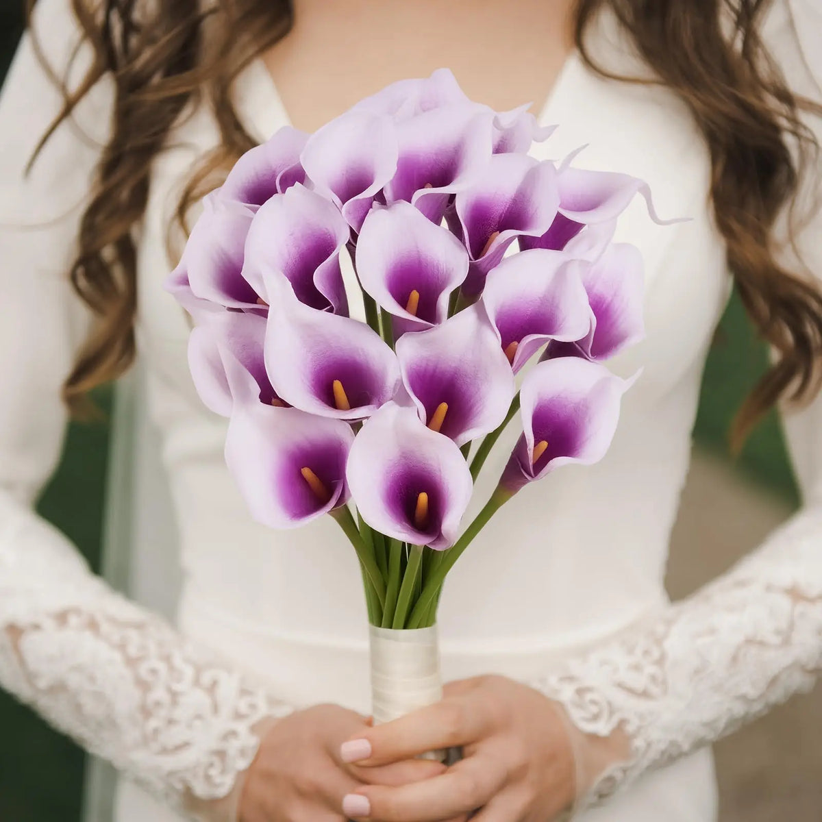 A bouquet of six artificial purple calla lilies held by a person wearing a white dress.
