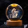 A spherical crystal ball with a gold glow features a laser engraved image of a lion and a lamb against a dark background.