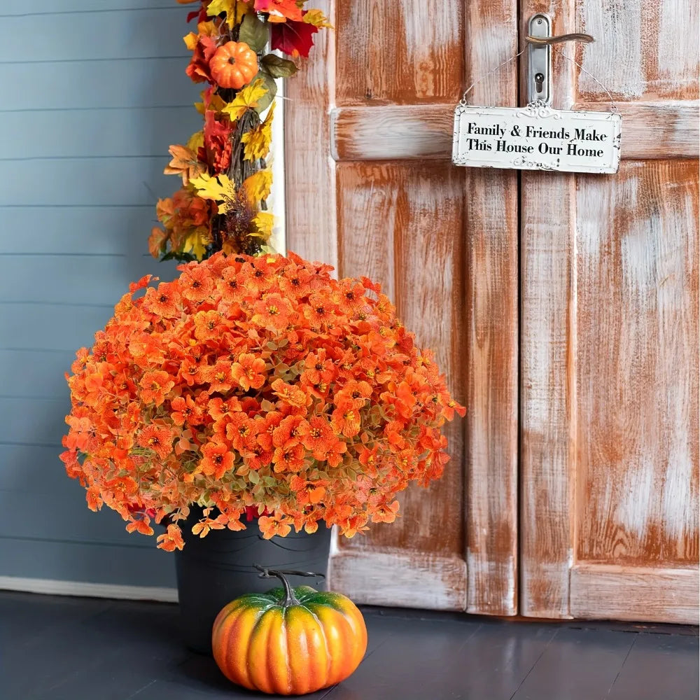 An artificial fall floral decor set featuring bright orange chrysanthemums and a pumpkin displayed on a wooden door.